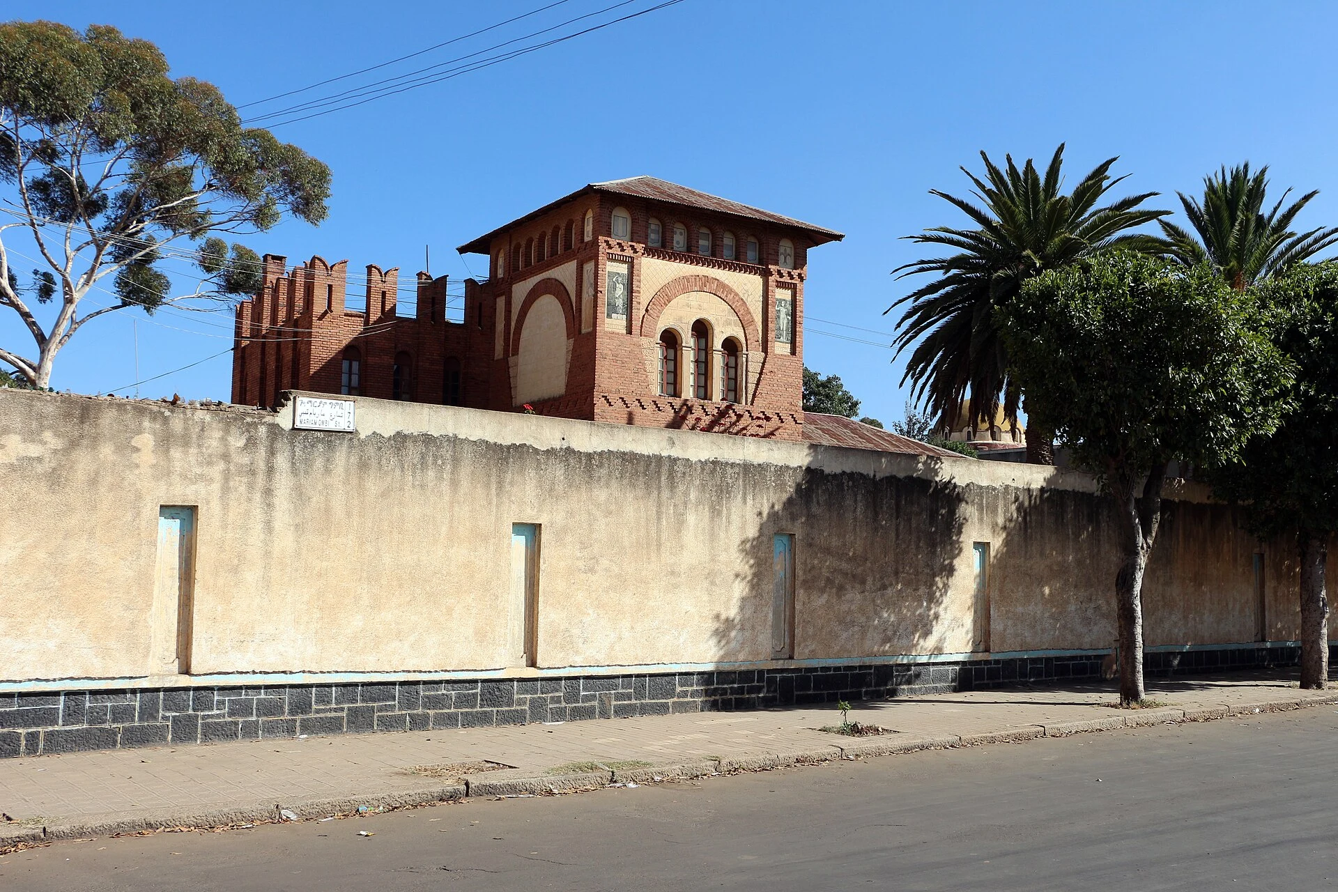 Straße in Asmara mit Geschäften des Viertels und religiösen Silhouetten im Hintergrund.