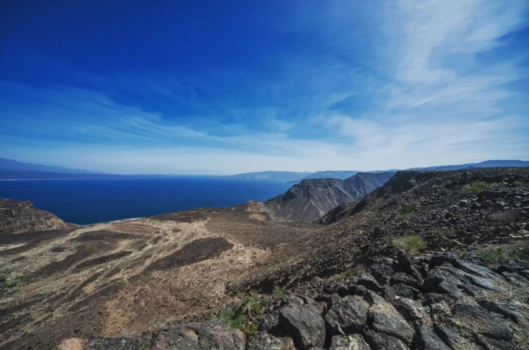 Panorama de Ghoubbet al-Kharab com costa vulcânica escura e Ilha do Diabo.