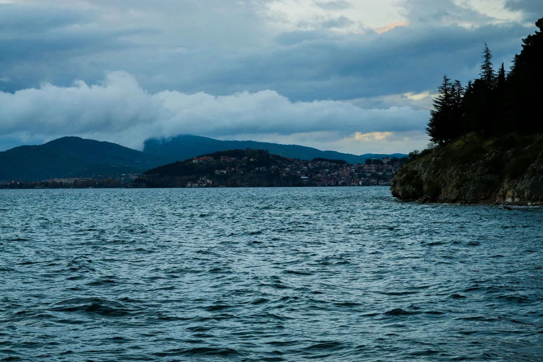 Ohridsee mit einer Stadt und Bergen unter bewölktem Himmel.